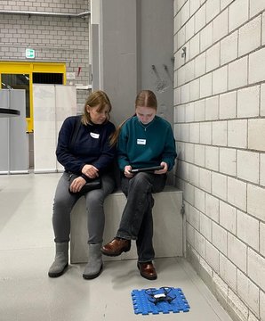 Due persone siedono in una stanza con pareti di mattoni e guardano un tablet.